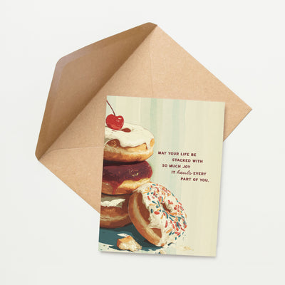 Greeting card with donuts and a cherry on top, featuring a motivational quote, next to an open brown envelope.